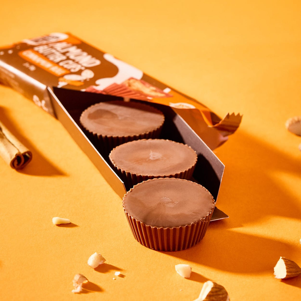 Bio Almondbutter Cups Cinnamon Roll in offener Packung mit Zimtstange und Mandelsplittern