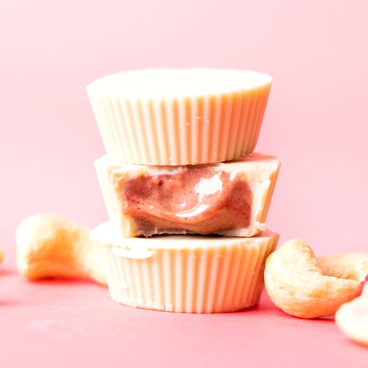 Gestapelte Bio Nutbutter Cups Mixed Box mit Cashewkernen auf rosa Hintergrund
