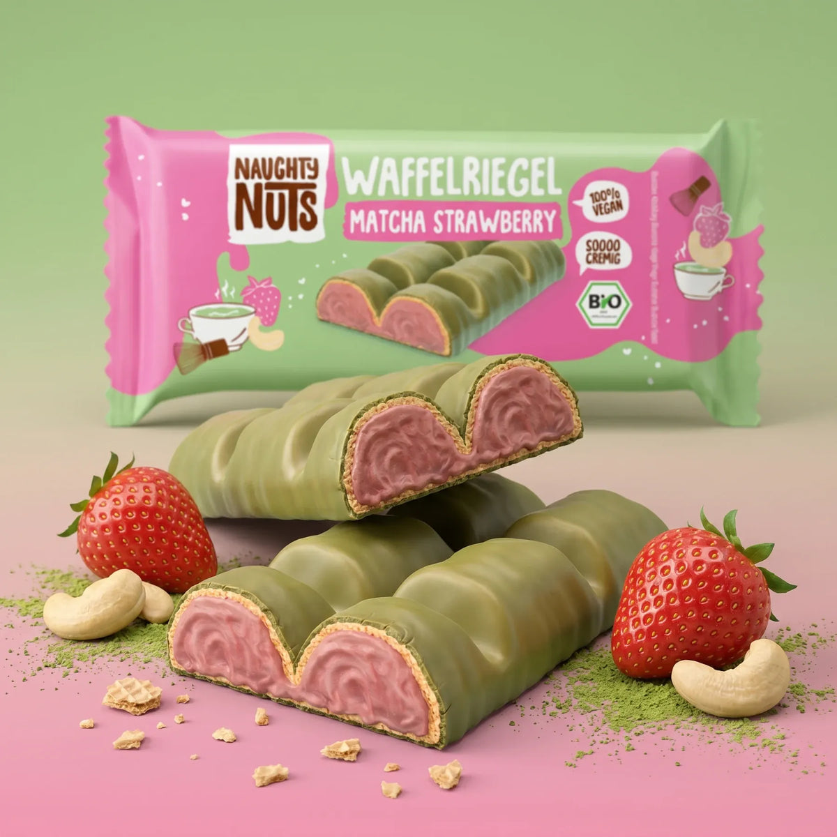 Waffelriegel Matcha Strawberry, grün umhüllt mit rosa Füllung, daneben Erdbeeren und Cashewkerne